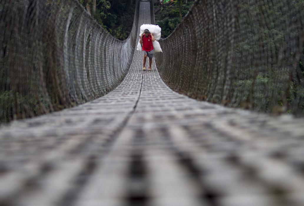 زن کشاورز در حال عبور از پلی معلق در نپال