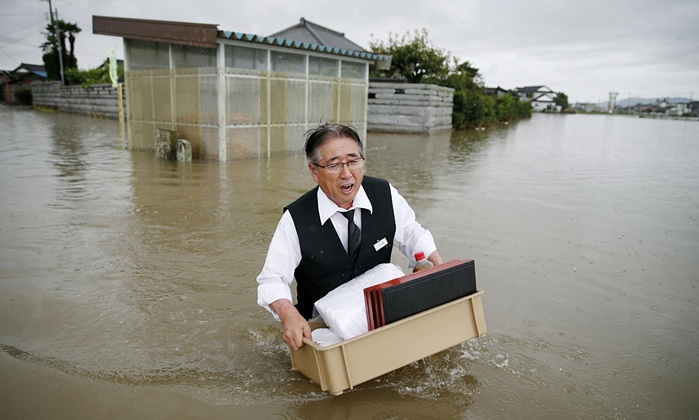 مرد ژاپنی در حال حمل وسائل شخصی خود از میان خیابان سیل گرفته شهر اویاما